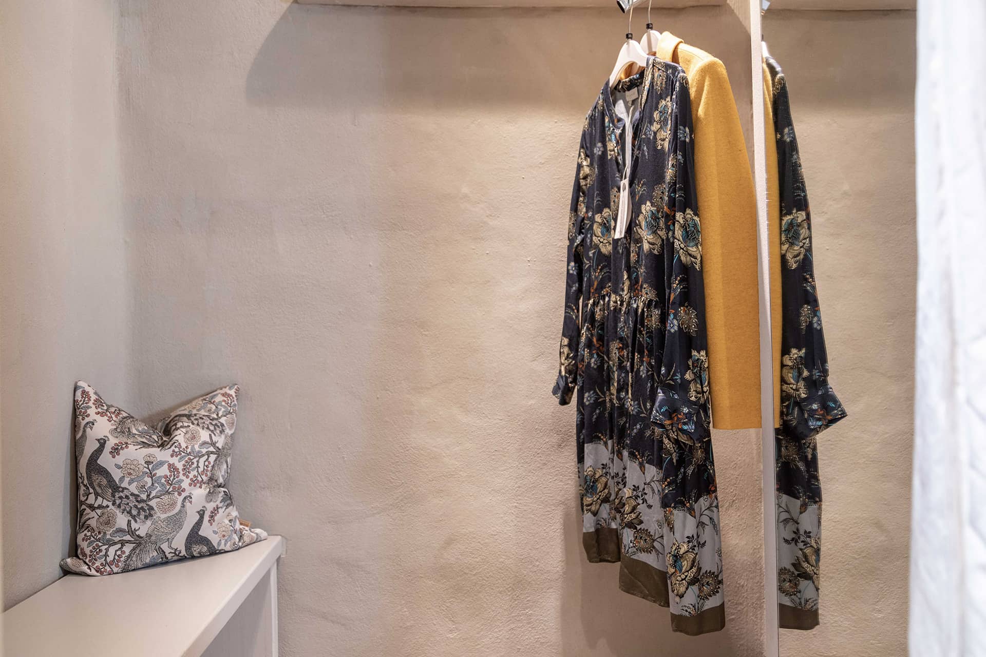 Ambientefoto: gemütliche Umkleidekabine mit lehmgeputzter Wand, einladender Sitzbank und modischer Kleiderauswahl